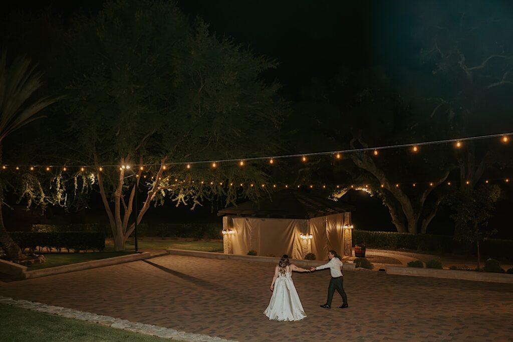 A bride and groom take a moment to dance alone together at their wedding reception in California.  Overhead there are string lights lighting their dance floor. 