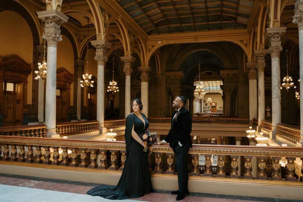 groom looking over at his bride in all black wedding attire on the top floor atrium