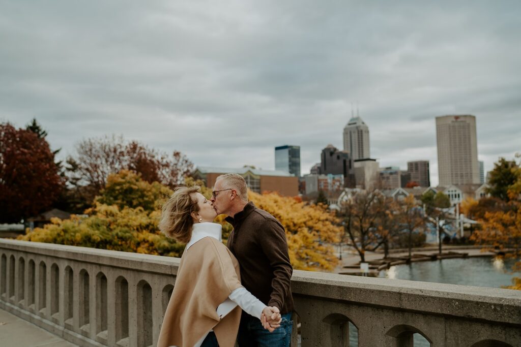 couple kissing on bridge in the fall with the indianapolis canal and skyline in the background