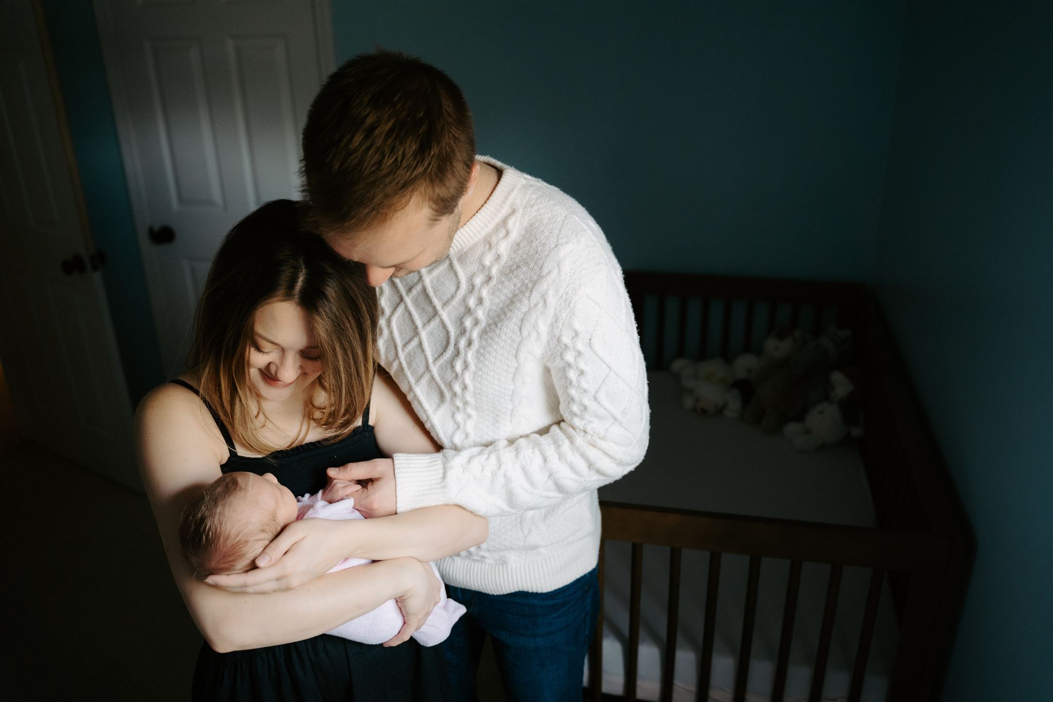 couple hugging together looking down at newborn baby in moms arms
