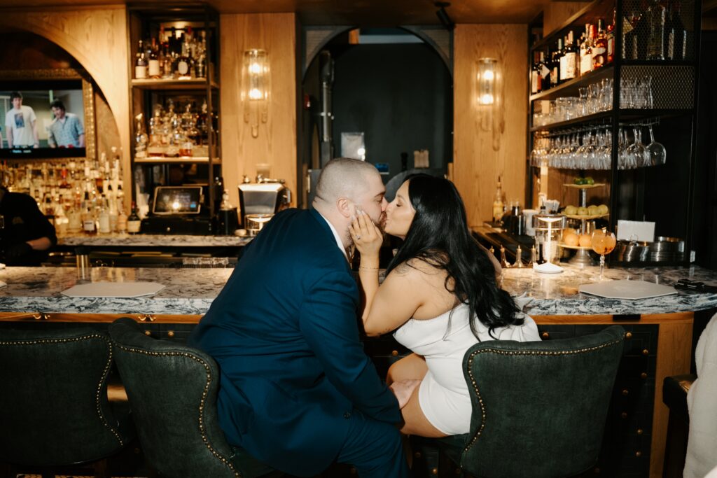 well dressed couple kissing at a bar while sitting in green chairs