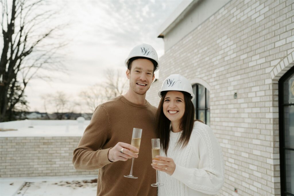 couple holding champagne flutes while wearing hard hats at their wedding venue