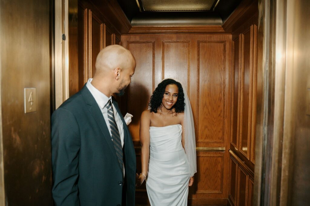 bride and groom smiling at one another in a elevator 