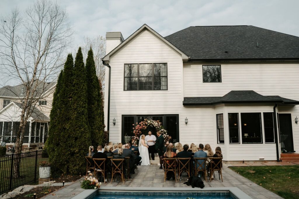 couple saying vows in the backyard by the pool with family