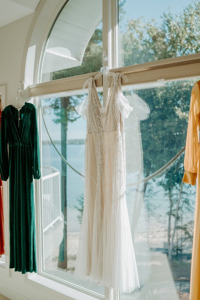 wedding dress hanging from window with bridesmaids dress