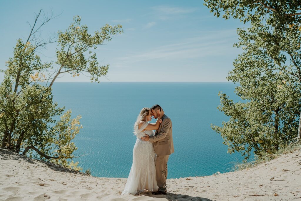 couple with their heads touching on the sand dunes and lake in background