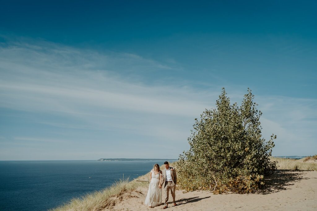 wedding couple walking on sand dunes on a clear sky