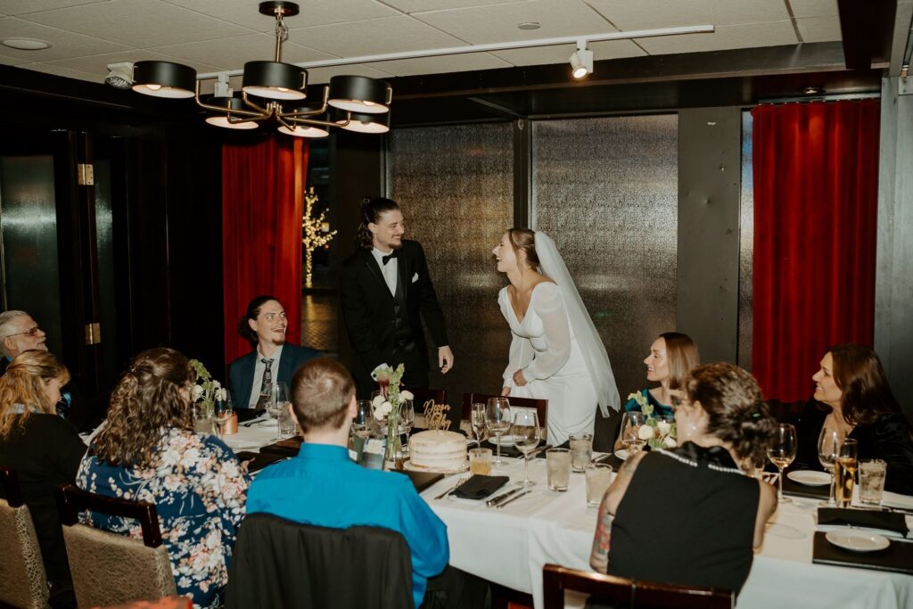 bride and groom standing while laughing with family at dinner